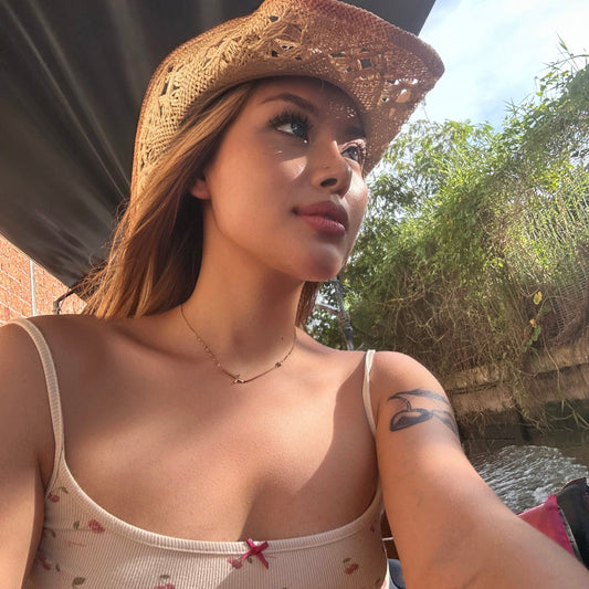 a person wearing a straw hat and a light floral-patterned top with thin straps