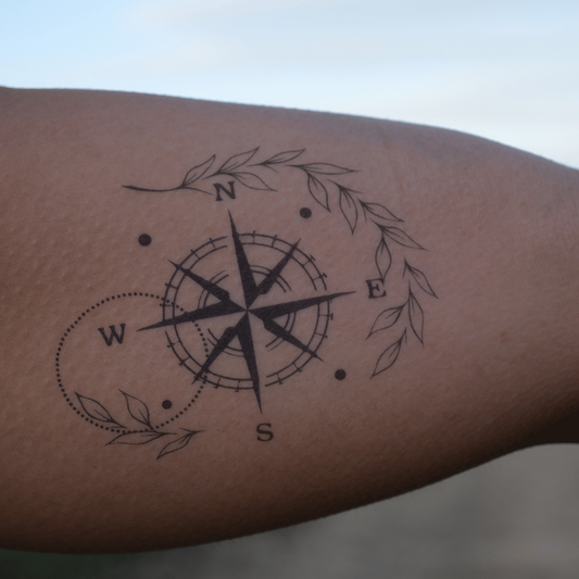 Minimalist compass tattoo symbolizing direction and exploration, adorned with delicate leaf accents.