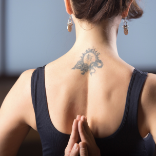 A black tattoo of a tribal-style design with a sun motif on the upper back, centered below the neck.