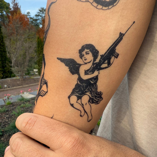 SteezyInk Angel Blicky temporary tattoo. Cherub holding rifle, black ink design, skin-safe semi-permanent tattoo.