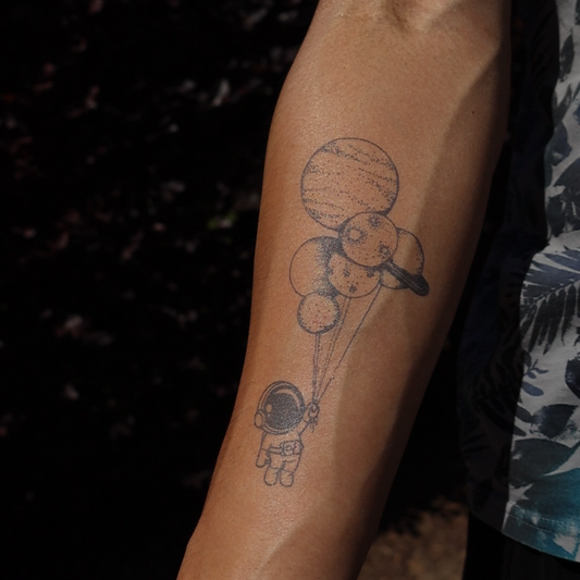 Zero-Gravity Temporary Tattoo on arm, astronaut holding planets design, Pure Black Ink™, 3 x 6 inch.