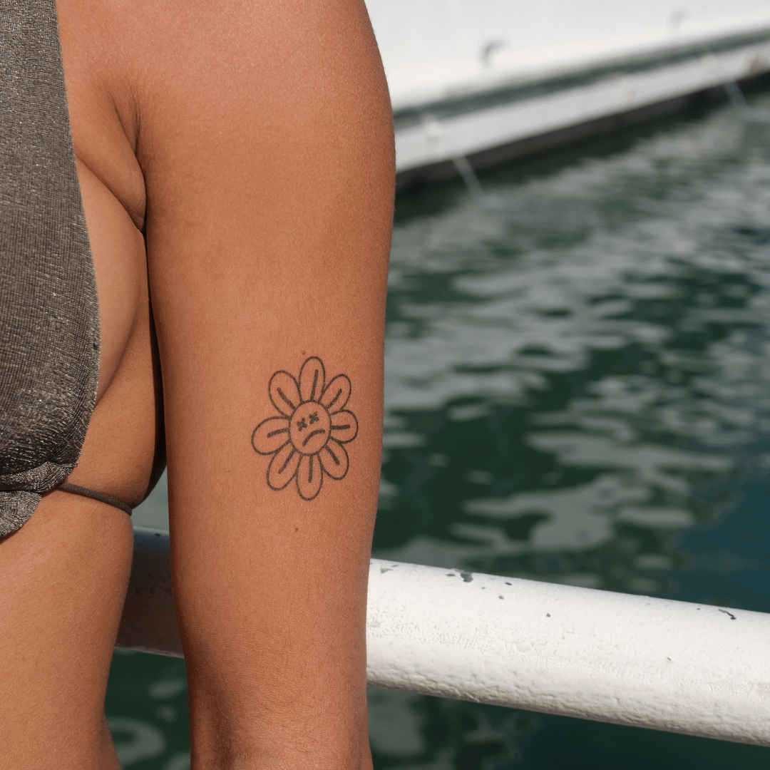 SteezyInk Sad Flower Temporary Tattoo on arm. Black outline daisy with a sad face design, two-week temporary tattoo.