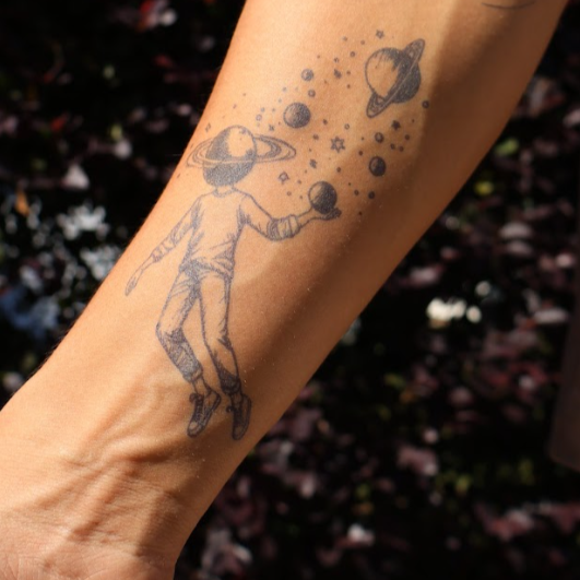 Orbiting Thoughts temporary tattoo on arm, space-themed design with planet head and stars.
