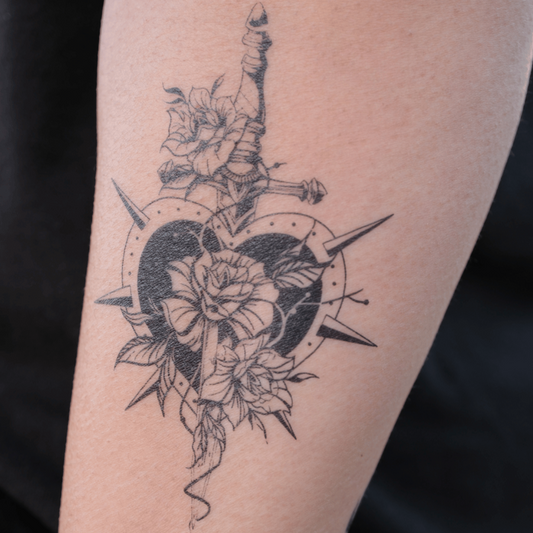 A heart-shaped tattoo with roses, a sword, and spiked details.