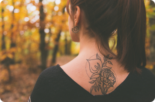 A minimalist floral tattoo on the upper back, featuring roses and leaves with dotted geometric accents.