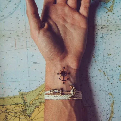 A minimalistic wrist tattoo featuring a compass design with cardinal directions