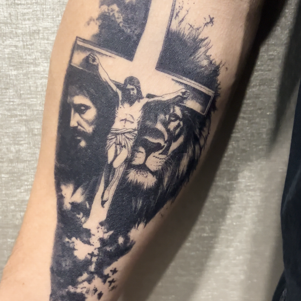 A complex and richly symbolic forearm tattoo is depicted, rendered entirely in black and gray ink. The design seamlessly blends several powerful Christian motifs with natural imagery, creating a deep narrative.

At the heart of the composition is a large, prominent cross, forming the primary structural element against which other figures are layered. The cross is depicted in a traditional Latin cross shape, with the vertical beam extending upwards and downwards, and the horizontal beam stretching across. It